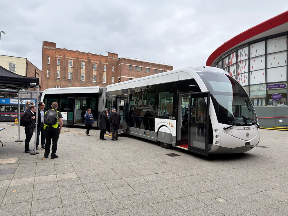 Modern articulated bus parked at a bus station with people standing nearby