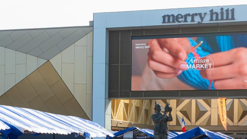 Exterior of Merry Hill building with a digital screen advertising an Artisan Market, and a statue in front