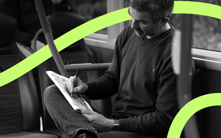 Person sitting on a bus seat, writing on a newspaper with a pen