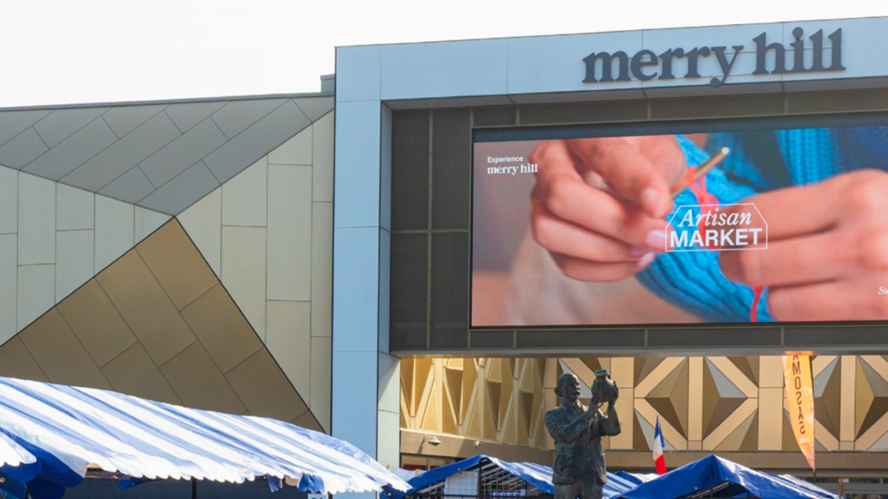 An image of the outside of Merry Hill shopping centre in Dudley, displaying a large advertisement for their 'Artisan Market'