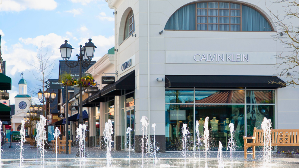 An image of McArthurGlen Designer Outlet West Midlands, with multiple shops in the background and fountains in the foreground.
